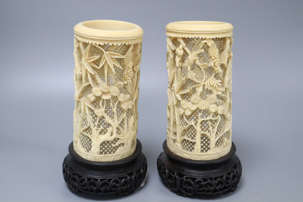 A pair of Japanese carved and pierced ivory brush pots, on hardwood stands, height 20cm